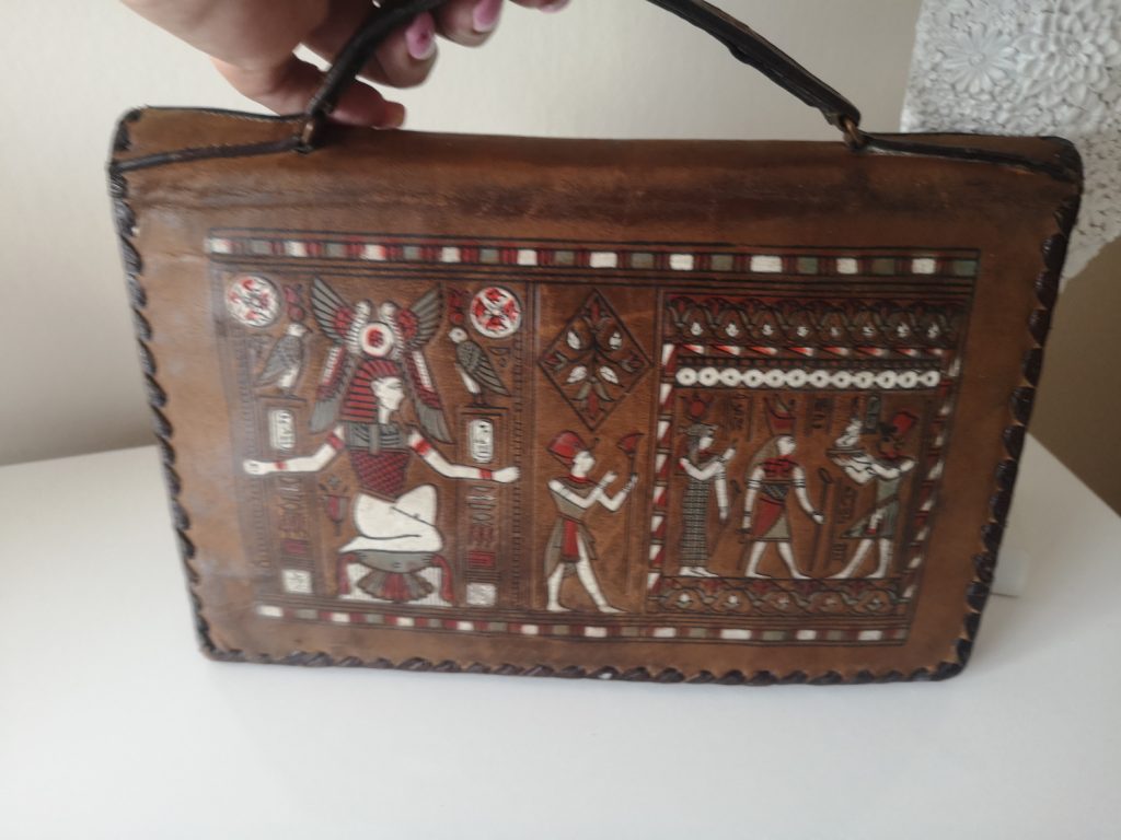 A leather handbag features beautiful and intricate decoration of Egyptian symbols and imagery. 